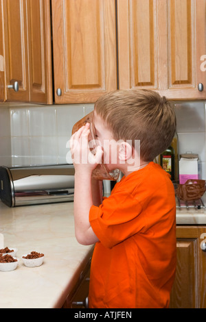 Ragazzo giovane leccare ciotola pulita dopo la produzione del cioccolato crispies Foto Stock