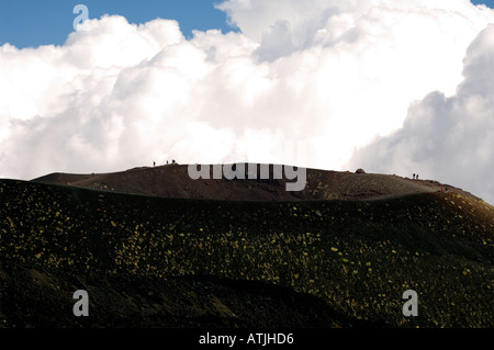 Piccole figure umane esposto contro le nuvole sul bordo di un piccolo cratere laterale di cenere nera sul Monte Etna Sicilia Foto Stock