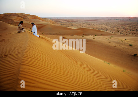 Due Bedu tribesmen in tradizionale abito dishdasha sulla sommità del desert dune di sabbia in Ramlat Al Wahaybah al tramonto Oman Foto Stock