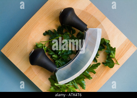 Prezzemolo a foglia piatta con una mezzaluna e tagliere in legno Foto Stock