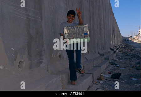 Un ragazzo tenendo una gabbia sorge accanto alla parete in Al Ram Gerusalemme Foto Stock