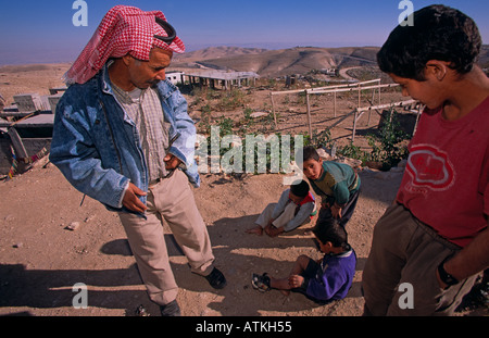 Giovani ragazzi beduino giocando a terra mentre un uomo Beduino e ragazzo adolescente guarda su Foto Stock