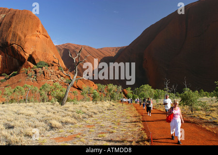 I turisti a piedi lungo il percorso circolare in inizio di mattina di sole a Ayers rock Uluru Territorio del Nord Australia Foto Stock