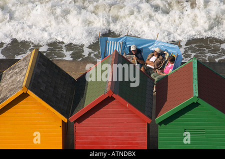 Tre persone a prendere il sole vicino alla pittoresca spiaggia di capanne a Whitby, North Yorkshire, Inghilterra. Foto Stock
