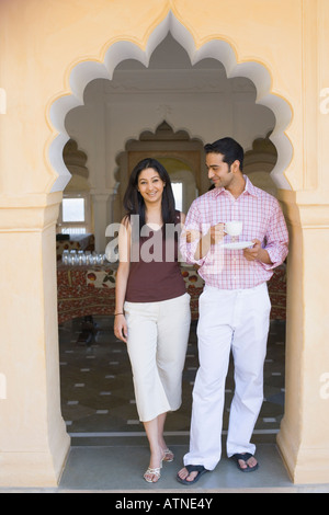 Ritratto di una giovane donna in piedi a braccetto con un giovane uomo con una tazza di tè con piattino Foto Stock