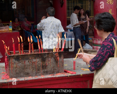 Donna accendendo candele per buona fortuna presso un santuario durante il Nuovo Anno Cinese a Bangkok Foto Stock