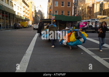 Un senzatetto uomo attraversa la Eighth Avenue nel quartiere di NYC di Chelsea con i suoi effetti personali su carrelli di shopping Foto Stock