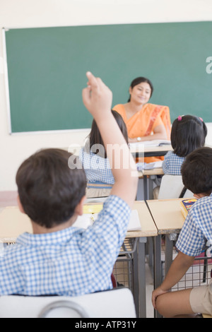 Vista posteriore di uno scolaro in una classe con la mano alzata Foto Stock