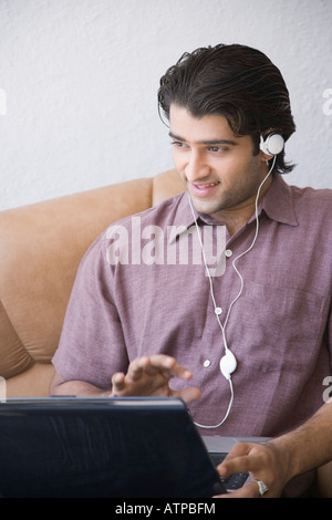 Giovane uomo seduto in poltrona e utilizzando un computer portatile Foto Stock