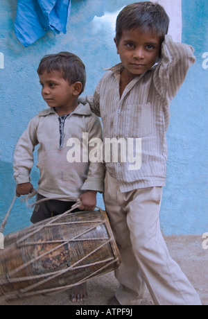 Due giovani fratelli giocando un tamburo su una strada del villaggio in India rurale. Foto Stock