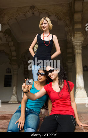 Due giovani donne di scattare una foto con il loro amico in piedi dietro di loro, Taj Mahal, Agra, Uttar Pradesh, India Foto Stock