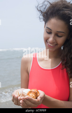 Close-up di una giovane donna holding conchiglie sulla spiaggia e sorridente Foto Stock