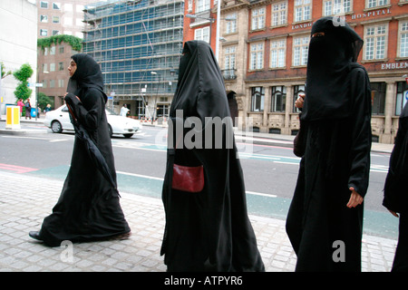 Tre donne a camminare su una strada di Londra su un viaggio di shopping vestita di nero in burka uno portante una borsetta Foto Stock