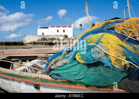 Rete da pesca impilati su barche da pesca sulla spiaggia con la Chiesa cattolica in background su isola di Mozambico Foto Stock