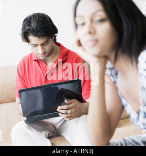 Close-up di una giovane donna di pensare con un giovane uomo che utilizza un computer portatile accanto a lei Foto Stock