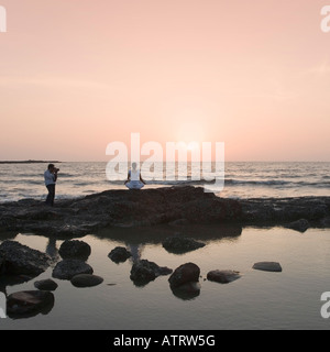 L uomo per catturare una donna fare yoga sulla spiaggia Foto Stock