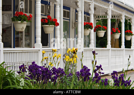 Rosso dei gerani in cestelli appesi sul portico bianco con Giallo e viola Iris nella porta anteriore County Wisconsin Foto Stock