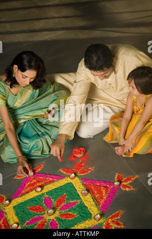 Angolo di alta vista di una metà uomo adulto e una giovane donna fare rangoli con la loro figlia Foto Stock