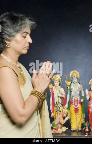 Profilo laterale di una donna matura pregando davanti di statue di Dio Foto Stock