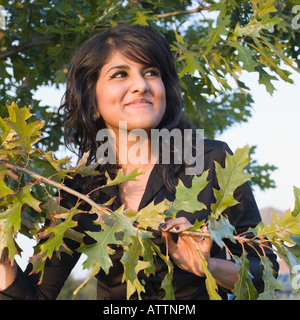 Close-up di una giovane donna in piedi accanto ad un albero e smirking Foto Stock
