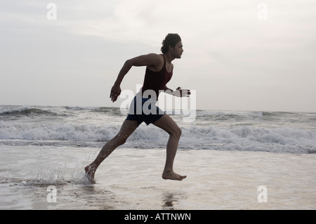Profilo laterale di un giovane uomo che corre sulla spiaggia Foto Stock