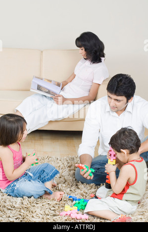 Metà uomo adulto a giocare con i suoi figli e la sua moglie leggendo una rivista in background Foto Stock