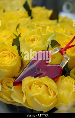 Rosso cuore di vetro in un mazzo di rose di colore giallo Foto Stock