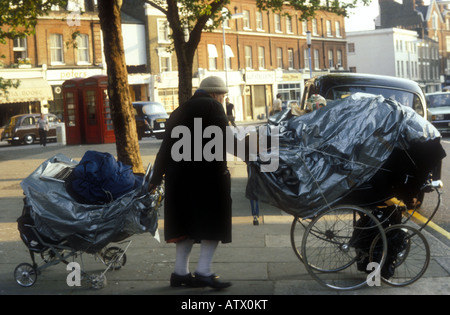 Donna senzatetto spingendo la sua carrozzina attraverso le strade di Chelsea, Londra Foto Stock