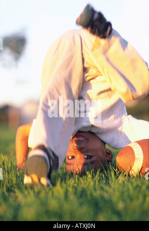 6 anno vecchio African American boy tenta headstand nel parco di erba Foto Stock