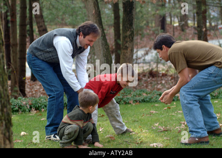 Elementi maschio di una famiglia estesa di giocare a calcio nel loro cortile anteriore sul giorno del Ringraziamento Foto Stock