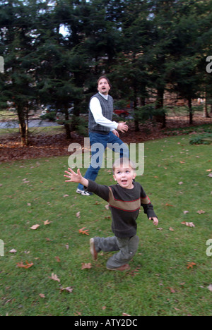 Elementi maschio di una famiglia estesa di giocare a calcio nel loro cortile anteriore sul giorno del Ringraziamento Foto Stock