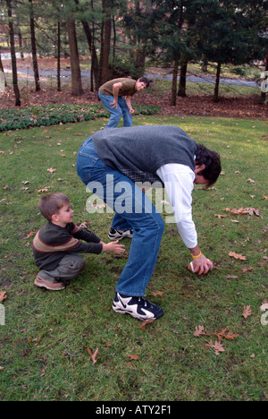 Elementi maschio di una famiglia estesa di giocare a calcio nel loro cortile anteriore sul giorno del Ringraziamento Foto Stock