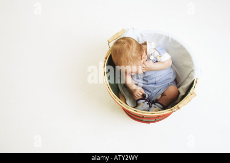 Un bambino si accorcizzò e sedeva in un cestino nello studio. Foto Stock