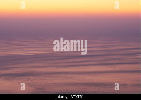 Alba rottura con golden colori caldi su una calma oceani superficie con dolci increspature Foto Stock
