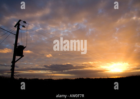 Palo elettrico trasformatore e fili stagliano cavi tramonto portano a sun suggerendo di energia solare Foto Stock