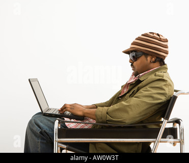 Vista laterale di African American metà uomo adulto che indossa un cappello e la digitazione sul computer portatile Foto Stock