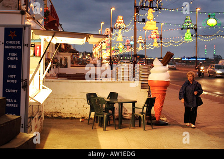 Una donna camminare davanti a un fast food chiosco sulla passeggiata di notte in Blackpool, Regno Unito Foto Stock