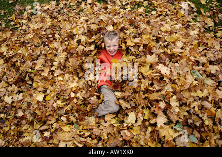 Nove-anno-vecchio ragazzo nel fogliame di autunno Foto Stock