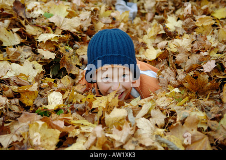 Nove-anno-vecchio ragazzo nel fogliame di autunno Foto Stock