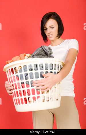 Giovane donna in piedi con piena Basket lavanderia lei s sembra arrabbiato vista frontale Foto Stock