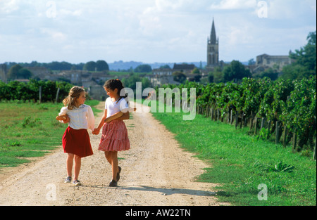 Due ragazze della scuola a piedi attraverso i vigneti con baguette vicino al villaggio di St Emilion in Francia Foto Stock