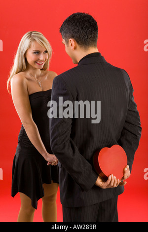 Giovane uomo in tuta è nascondere scatola di cioccolatini prima di bella donna sorridente l uomo è in piedi indietro Foto Stock