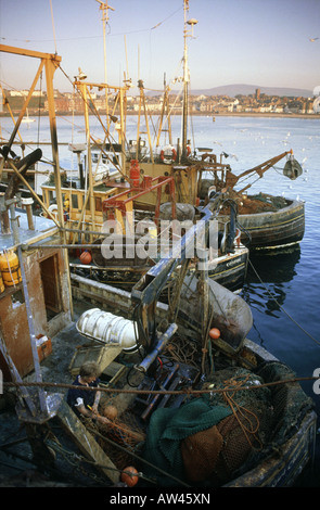 La flotta da pesca barche ormeggiate nel porto di Molo Ponte di parete caricato con reti di marcia verricelli uomini al lavoro Foto Stock