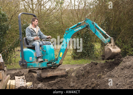 Un uomo alla guida di un mini escavatore / escavatore Foto Stock