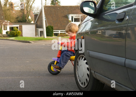 Bimbo di 2 anni in bici in pericolo sulla strada tirando fuori da dietro un'auto. Foto Stock