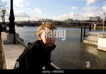 Ragazzo (Gioventù) seduto sul terrapieno, Thames, London REGNO UNITO cercando pensieroso Foto Stock
