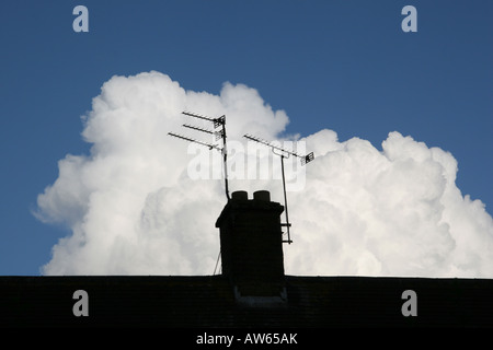 White cumulo nimbus nuvole sopra costruzione stagliano tetto con camino e antenna televisiva Foto Stock