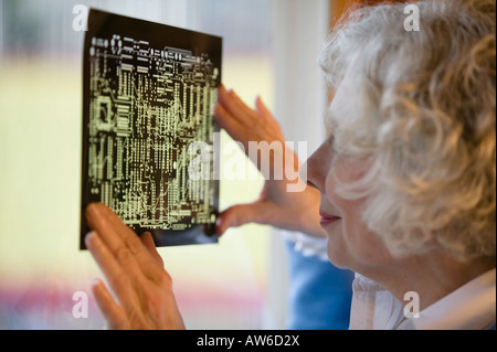 Senior donna cerca su una scheda a circuito stampato maschera Foto Stock