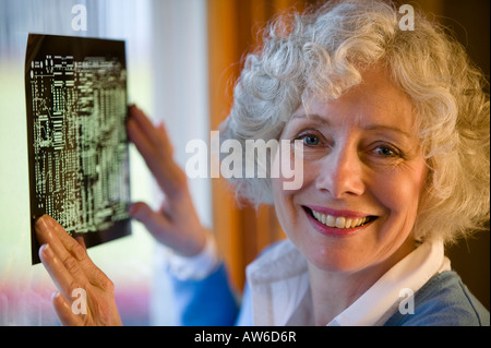 Senior donna cerca su una scheda a circuito stampato maschera Foto Stock