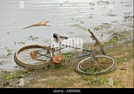 Vecchio arrugginito bici abbandonate che giace accanto al canal Foto Stock